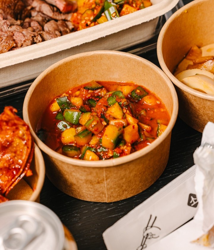 A close-up shot of a paper bowl of cucumber kimchi from Sopo.