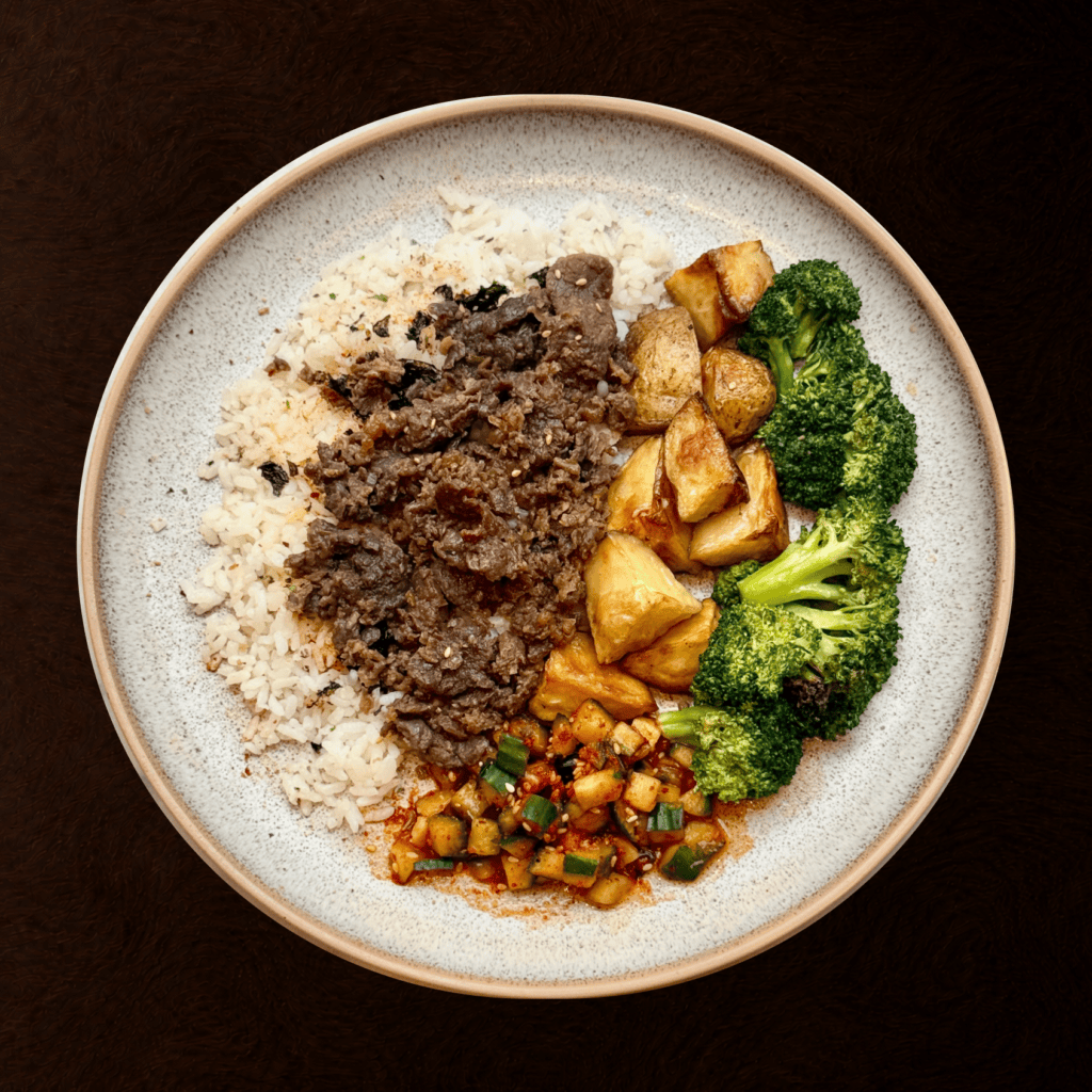 A build-your-own Korean plate with purple rice, beef bulgogi, kimchi, and house sauce, packed for delivery